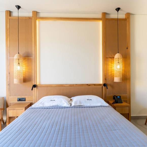 Junior suite with a double bed with wooden headboard wall, pendant lights and a pair of wooden chairs each on either side