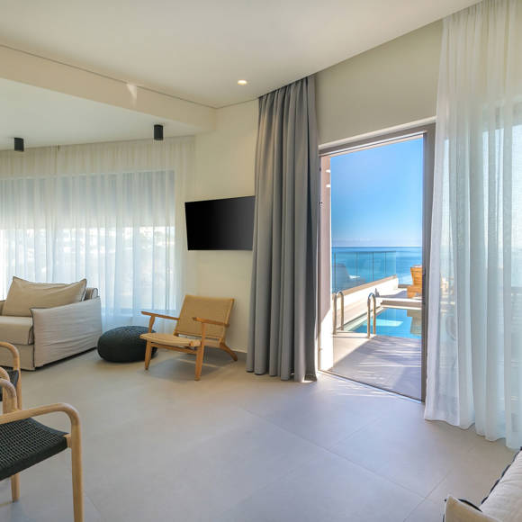 Suite's cozy living room with modern furniture, wall-mounted TV and access to the terrace with the private pool
