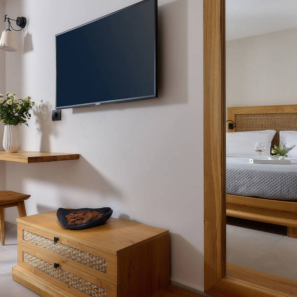 Bedroom with a wall-mounted TV, a wooden desk and chair and a mirror with the reflection of a double bed