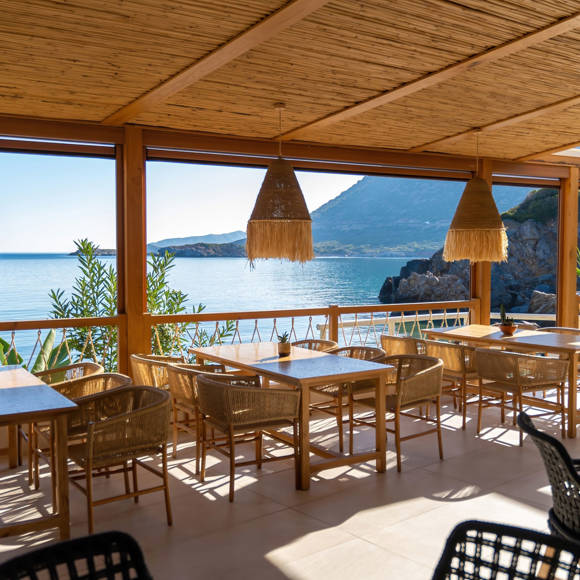 Seafront dining area at Mambo Beach Restaurant with wooden furniture, woven lighting and panoramic coastal view