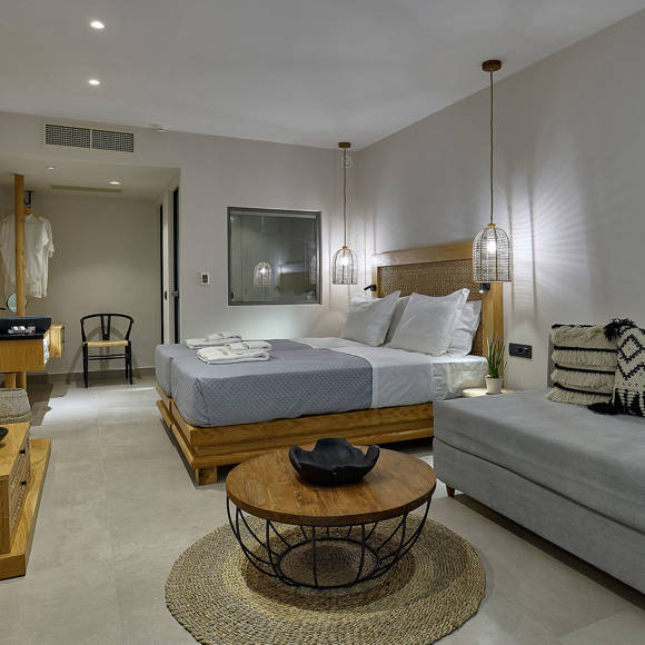 Junior suite with double bed, sofa with patterned cushions, wooden furniture, and a round coffee tables