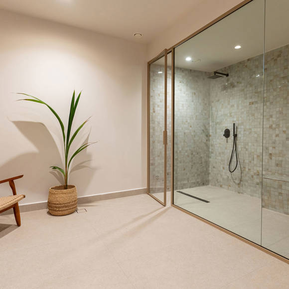 Spa shower area with mosaic tiles, glass partition and natural decor elements